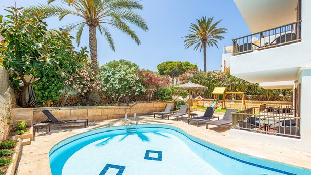 A swimming pool with lounge chairs, surrounded by palm trees and a building with a balcony. - "Gran Sol Family 1" Apartment with Shared Pool, Wi-Fi, and Air Conditioning (Tourist Tax Included) (Felanitx)