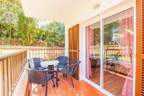 Un balcon doté de meubles en osier, d’une porte vitrée et offrant une vue sur un jardin.