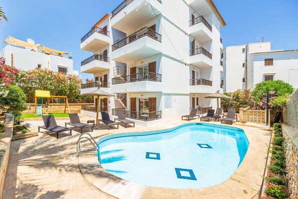 A multi-story hotel with a swimming pool, lounge chairs, and a covered seating area.