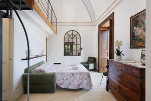 Une chambre à coucher avec un lit, une commode, une chaise, une plante et un tableau accroché au mur.