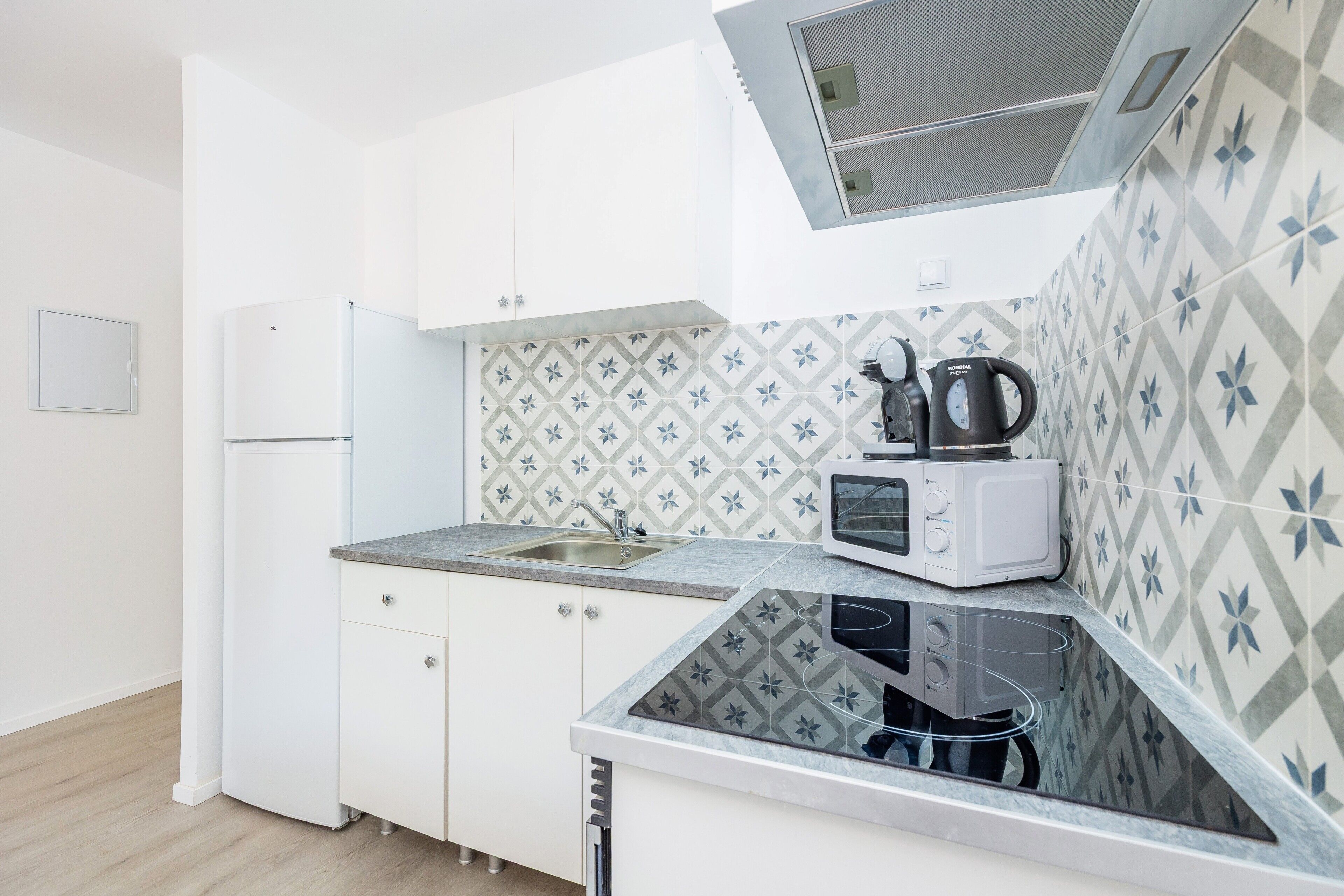 A kitchen with white cabinets, a sink, a microwave, and a kettle.