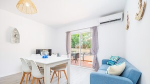 Un salon moderne avec une table à manger blanche, un canapé bleu et une grande porte-fenêtre coulissante donnant sur une terrasse extérieure.