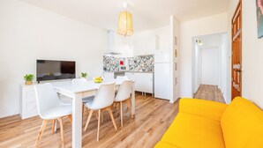 Una cocina moderna con armarios blancos, una mesa de comedor con sillas, un televisor y un sofá amarillo brillante.