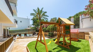 Un patio con un columpio, una piscina y un edificio blanco.
