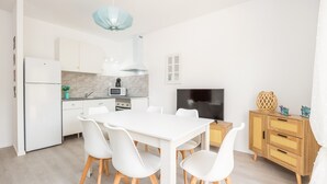 Uma cozinha moderna com armários brancos, uma mesa de jantar com cadeiras, uma televisão e um aparador de madeira com objetos decorativos.