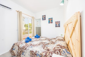 A bedroom with a bed, a wooden headboard, a balcony with curtains, and wall art.