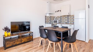A modern kitchen with a tiled backsplash, a wooden dining table with chairs, a flat-screen TV on a wooden console, and a white refrigerator. - Apartment "Gran Sol Family 7" with Shared Pool, Wi-Fi, Air Conditioning (Tourist Tax Included) (Felanitx)