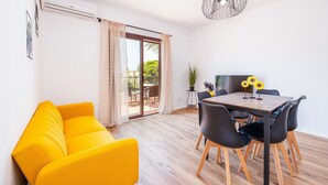 A bright yellow sofa, a wooden dining table with black chairs, and a large window with curtains. - Apartment "Gran Sol Family 7" with Shared Pool, Wi-Fi, Air Conditioning (Tourist Tax Included) (Felanitx)