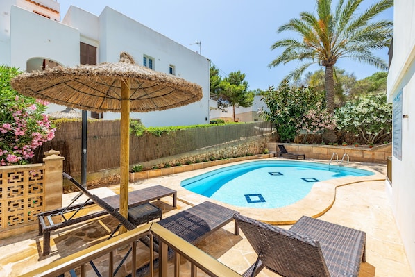 A swimming pool with lounge chairs and an umbrella, surrounded by a stone wall and greenery.