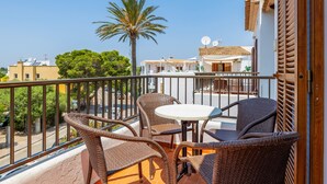 A balcony with wicker furniture, a white table, and a view of palm trees and buildings. - Apartment "Gran Sol Family 7" with Shared Pool, Wi-Fi, Air Conditioning (Tourist Tax Included) (Felanitx)