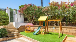 A children's play area with a slide, a small playhouse, and a staircase leading to a white building. - Apartment "Gran Sol Family 7" with Shared Pool, Wi-Fi, Air Conditioning (Tourist Tax Included) (Felanitx)
