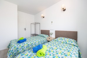 A hotel room with two beds, a nightstand, a wall-mounted shelf, and a wall-mounted lamp.