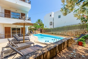 A swimming pool with lounge chairs, a thatched umbrella, and a stone wall.