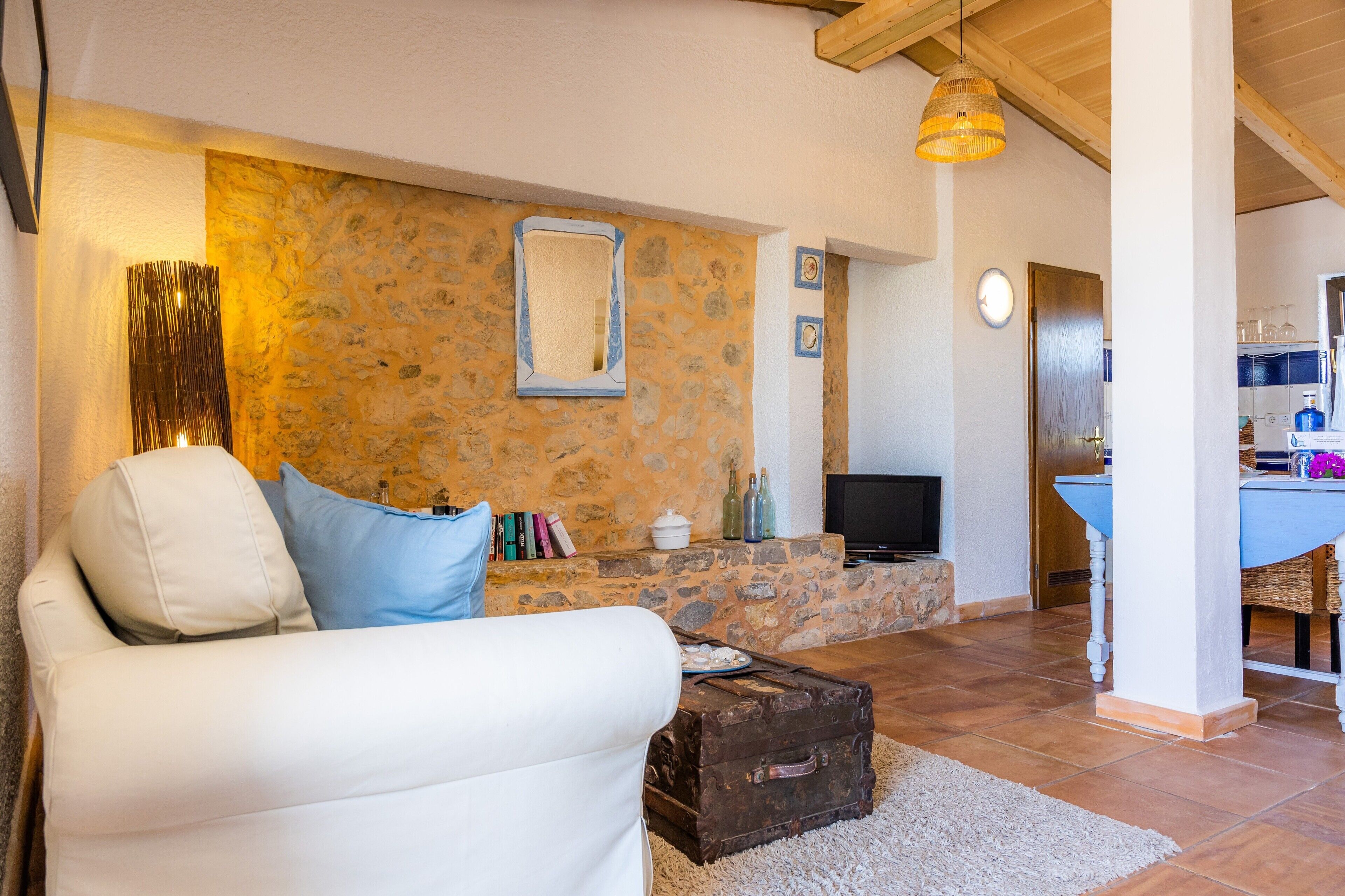 Ein Wohnzimmer mit Steinwand, einem weißen Sofa, einem Fernseher und einer Küchenzeile im Hintergrund.