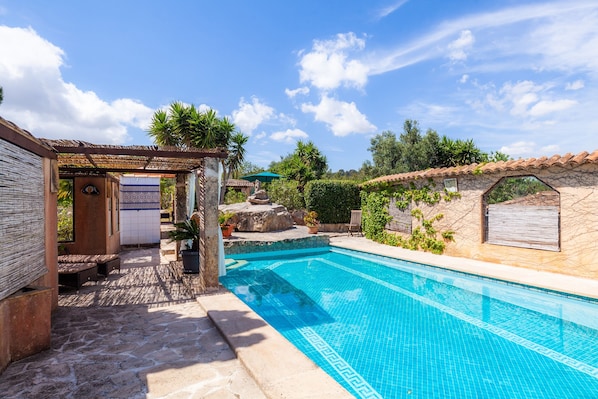 A swimming pool with a stone wall, a pergola, and a small seating area.