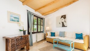 Sala de estar con sofá, una mesa de centro, aparador de madera, ventana con cortinas y un cuadro en la pared.