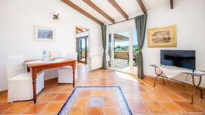 A room with a wooden table, chairs, a TV, and a view through a glass door.