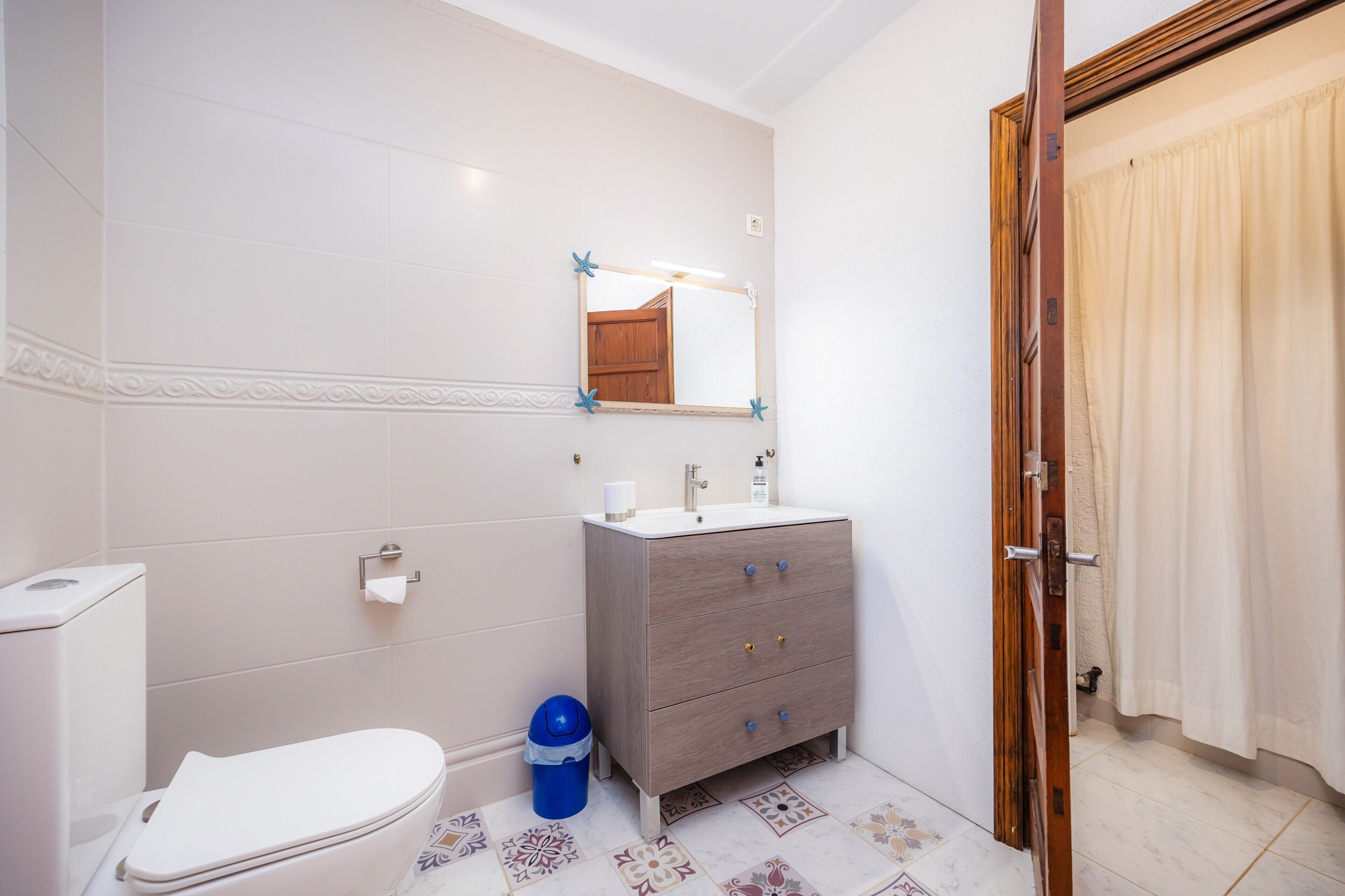 Un baño con inodoro, lavamanos, tocador, espejo y baldosas de suelo estampadas.