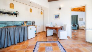 A kitchen with a tiled floor, wooden ceiling beams, a dining table with chairs, and a small refrigerator.