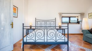 A bedroom with a metal bed frame, a window with a view, a green sofa, and a tiled floor.