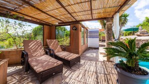 A covered outdoor seating area with wicker furniture, a potted plant, and a view of a pool and greenery. - Vacation Apartment "Individual Guesthouse Mallorca" with Mountain Views, Pool & Wi-Fi (Manacor)