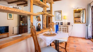 A rustic interior with exposed wooden beams, a dining table with a white tablecloth, a television, and a cabinet with various items. - Vacation Apartment "Individual Guesthouse Mallorca" with Mountain Views, Pool & Wi-Fi (Manacor)