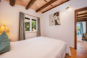 A bedroom with a bed, a window with curtains, a wall-mounted artwork, and a wooden ceiling.