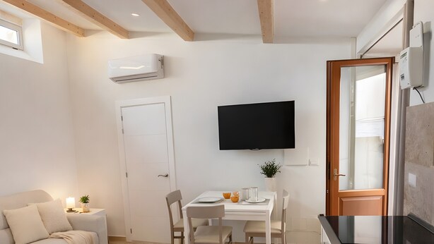 A modern kitchen with a dining area, a sofa, and a TV.