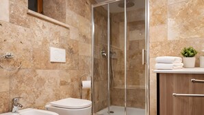 A bathroom with a shower, bidet, toilet, and a wooden cabinet.