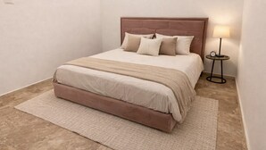 Un dormitorio con una cama, almohadas, una mesita de noche con lámpara y una alfombra.