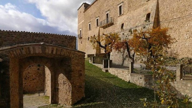 A stone building with a courtyard, a stone archway, and a tree with autumn leaves.