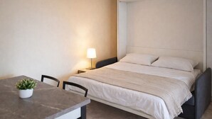 A single bed with a headboard, a bedside table with a lamp, a small potted plant, and a chair.