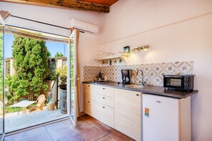 A compact kitchen with a built-in microwave, a small refrigerator, and a window overlooking a garden.