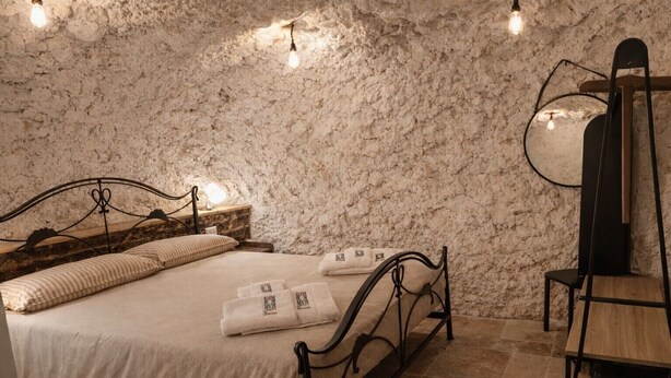 A bedroom with a stone wall, a bed with pillows, a bedside table with a lamp, and a chair. - Apartment 'Cafuorchie - Arco Pronti' with Mountain View, Wi-Fi and Air Conditioning (Sant'Agata di Puglia)