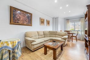 A living room with a beige sectional sofa, a glass-top coffee table, a small table with a checkered tablecloth, and a painting on the wall. - Apartment 'La Gimena ' with Balcony and Air Conditioning (Orihuela)