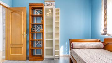 Un dormitorio con puerta de madera, armario con estantes múltiples, cama con colcha estampada y pared azul.