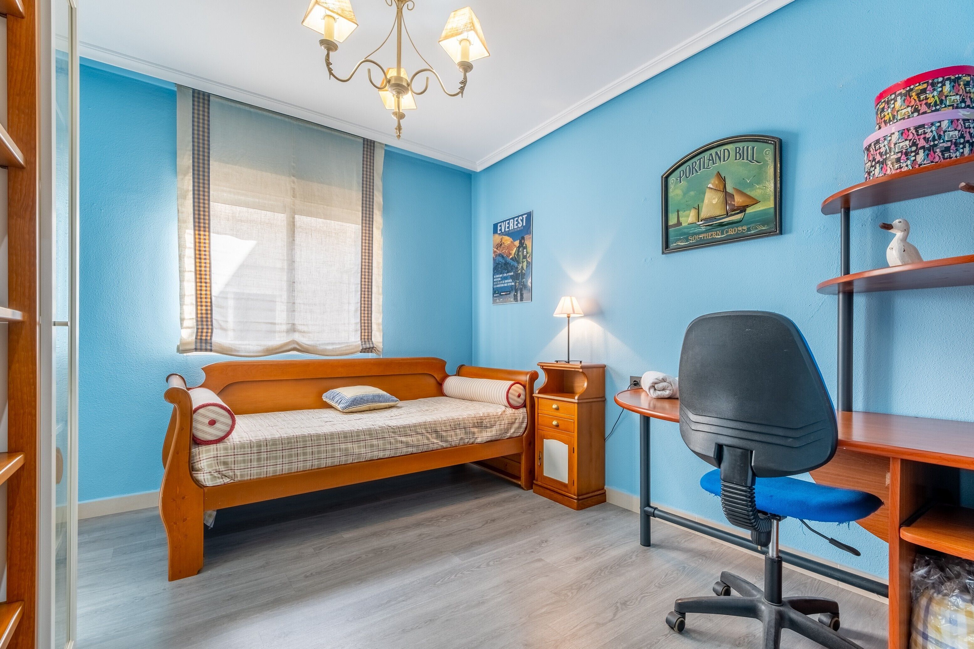Een kamer met een houten bed, bureau, stoel en een plank met decoratieve objecten.