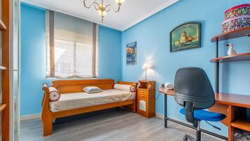 Een kamer met een houten bed, bureau, stoel en een plank met decoratieve objecten.