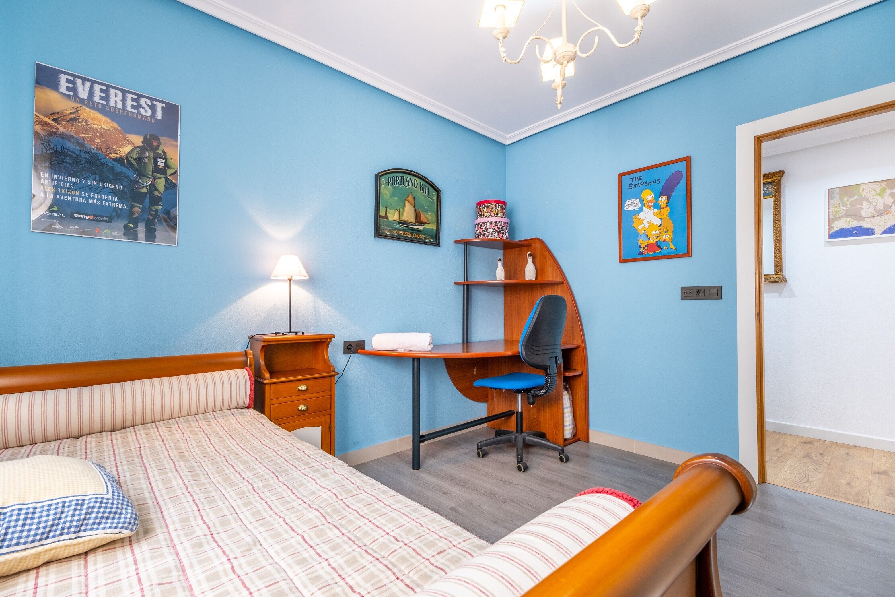Een slaapkamer met een bed, bureau, stoel en een poster aan de muur.