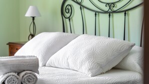 Un lit bien fait, avec des serviettes blanches pliées en rouleau, une tête de lit en métal et une lampe de chevet.