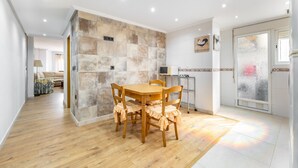 Un coin repas avec une table et des chaises en bois, un mur en pierre et un espace cuisine équipé d’un réfrigérateur.