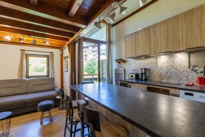 A modern kitchen with a central island, wooden cabinets, and a view of a building outside. - Manigod Merdassier Apartment 8 Guests, Shared Pool & Wi-Fi (Manigod)
