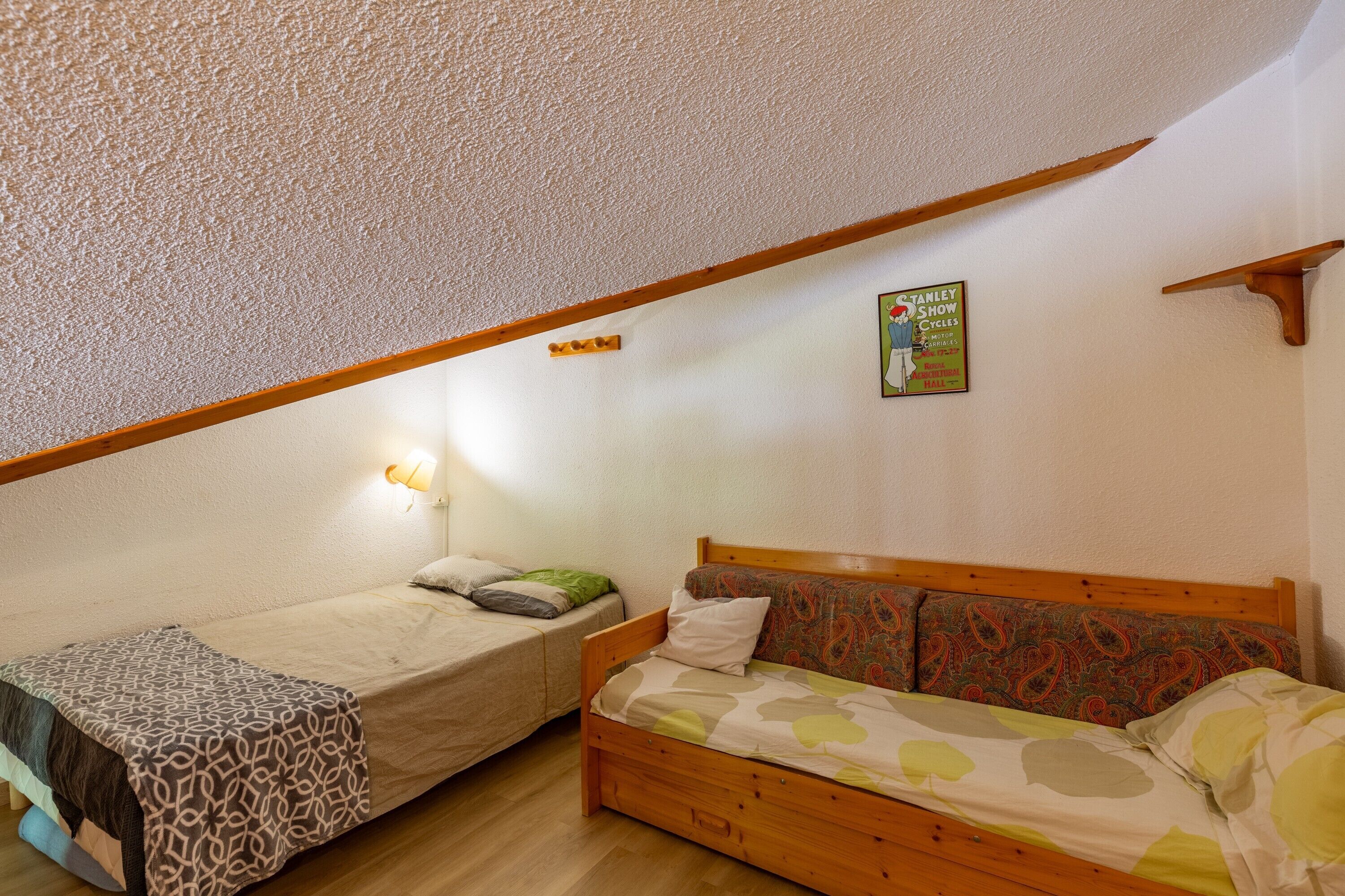 Une chambre avec deux lits, un plafond en bois, un luminaire fixé au mur et une affiche.