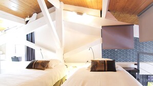 Une chambre d’hôtel avec deux lits, des poutres apparentes en bois au plafond, une grande fenêtre et une vue sur l’extérieur.