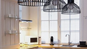 Et moderne køkken med hvide skabe, en mikrobølgeovn, elkedel og vask under et vindue med skodder.