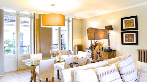 A modern living room with a glass dining table, white sofas, and a large window with a view of buildings.
