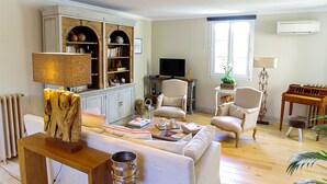 A living room with a sofa, two armchairs, a wooden cabinet with books, a television, and a radiator.