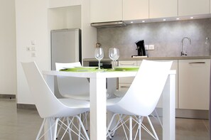 A modern kitchen with white cabinetry, a stainless steel sink, and a dining area with white chairs and a table. - Cheverus - Centre / 1 chambre avec ascenseur (Burdeos)