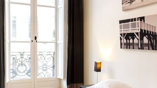 A hotel room with a bed, a nightstand, a lamp, a window with curtains, and a wall-mounted picture. - Condillac - Localisation exceptionnelle avec ascen (Burdeos)