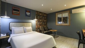 Een hotelkamer met een bed, nachtkastje, lamp, boekenplank en een kleintje tafel met stoelen.